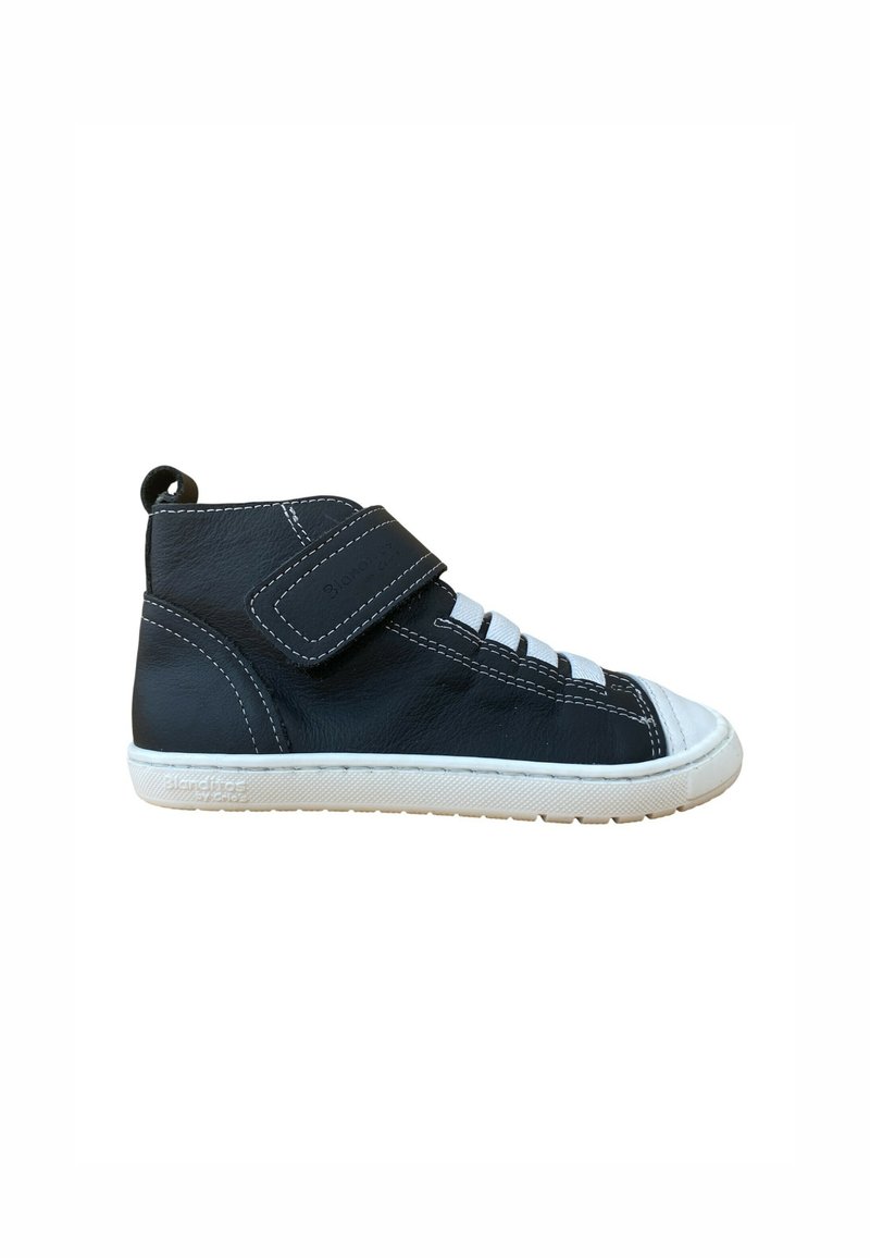 Zapatilla alta de cuero negro con punta y suela de goma blanca, que presenta una correa de Velcro y un diseño de cordones, con detalles de costuras en contraste.