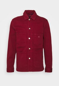 Veste en coton rouge avec col, quatre poches avant et boutons en métal. Elle présente un tissu durable et des coutures soigneusement réalisées.