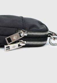 Sac en nylon noir avec double fermeture éclair et quincaillerie en acier inoxydable. Présente une texture lisse et élégante ainsi qu'un design compact, idéal pour transporter l'essentiel.