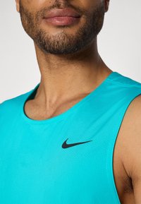 Turkoosi urheilutoppi, joka on valmistettu hengittävästä verkkomateriaalista. Vasemmassa rinnassa on musta Nike-logo ja pyöreä pääntie.