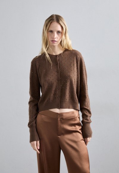 Cardigan court marron avec encolure ronde, manches longues et broderies décoratives. Associé à un pantalon en satin marron lisse.