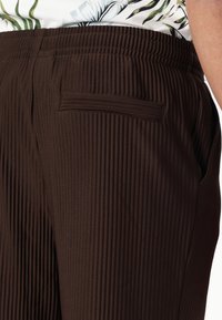 Pantalones de tela acanalada marrón con cintura elástica, bolsillos laterales y un bolsillo trasero, que presentan un diseño texturizado.