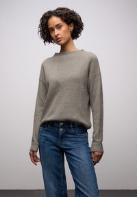 Vaaleanharmaa neulepusero, jossa leveä kaula-aukko, ribbineuloste ja rennon istuva malli, yhdistettynä sinisiin farkkuihin, joissa on viiden napin suljenta.