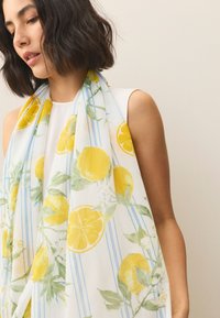 Lekka, przezroczysta chustka z wzorem cytryn i liści na białym tle z niebieskimi paskami. Miękki materiał o gładkiej fakturze.