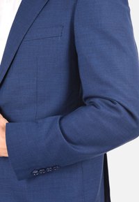 Blazer blu navy in tessuto testurizzato, con taschino sul petto e quattro bottoni decorativi sulle maniche. Vestibilità su misura con spalline strutturate.