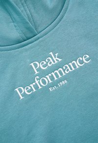 Lys blå bomulds sweatshirts med hvid tekst "Peak Performance" og "Est. 1986" nedenunder. Blød tekstur, rund halsdesign.