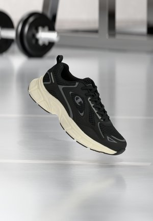 Black athletic shoe with mesh upper, white sole, and gray accents. Features a textured design and rounded toe, suitable for active use.