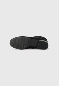 Semelle d'une botte cheville en cuir noir avec une bande de roulement en caoutchouc texturé et un petit talon bloc avec une bande grise contrastante.