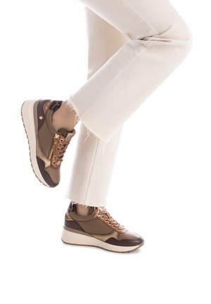 Braune Ledersneaker mit strukturierten Akzenten, goldenen Beschlägen und einer klobigen weißen Sohle, kombiniert mit hellen Jeans mit ausgefranstem Saum.