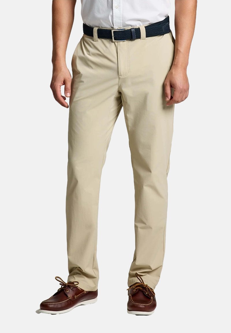 Pantalon en mélange de coton beige à coupe décontractée, avec une fermeture éclair, des poches latérales et une ceinture tissée marine. Complété par des chaussures bateaux marron.