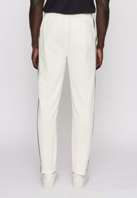 Hvite joggebukser med en innsvingt fasong, med svart sidestripe og elastisk midjebånd, kombinert med hvite sneakers.
