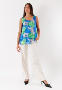 Top leggero senza maniche con sfondo blu, decorato con foglie di giglio verdi e fiori bianchi. Abbinato a pantaloni bianchi a gamba larga e tacchi neri.