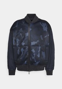 Blouson bomber bleu marine avec motif camouflage bleu foncé, fermeture éclair à l’avant, col, poignets et taille côtelés et manches unies bleu marine.