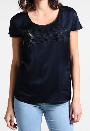 Haut bleu marine à manches courtes avec un panneau noir texturé sur la poitrine. Tissu lisse avec une coupe décontractée, associé à un jean bleu clair.