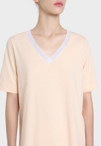 T-shirt di cotone pesco con maniche corte e scollo a V, caratterizzato da un bordo bianco decorato lungo il collo. Design semplice e senza fronzoli.