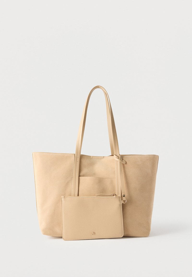 Μπεζ τσάντα ώμου από σουέντ με μακριές λαβές και προσαρτημένη τσαντάκι με φερμουάρ στο ίδιο χρώμα, σε απλό λευκό φόντο.