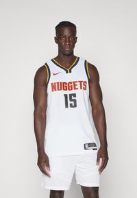 Biely basketbalový dres s nápisom "NUGGETS" a číslom 15 v žltej a námornej farbe. Má okrúhly výstrih, námorné a žlté lemovanie a je kombinovaný s bielymi šortkami.