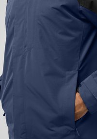 Veste bleu marine au design élégant, présentant une texture lisse, des poches latérales et un empiècement noir contrastant à l'épaule.