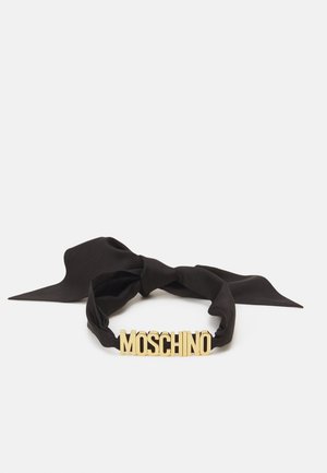 Black fabric headband with a large gold "MOSCHINO" logo at the front, featuring a bow-style design and smooth texture.