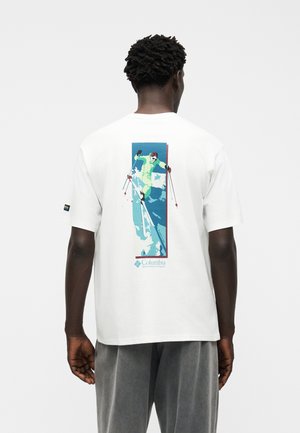 Homme portant un T-shirt blanc avec un graphisme coloré représentant un skieur descendant une pente enneigée, avec le logo Columbia Sportswear dans le dos.