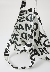 Borsa in cotone con lettere nere in grassetto su sfondo bianco. Presenta due manici e un design con apertura superiore, enfatizzando il testo grafico.