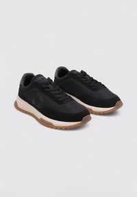 Zapatillas negras que presentan una combinación de materiales de tela y ante, punta redonda, diseño de cordones y una suela de goma marrón en contraste.