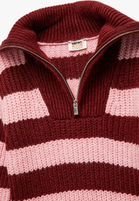 Pull en maille avec un col montant, présente des rayures horizontales bordeaux et roses, une fermeture éclair en métal, un tissu texturé et un col côtelé.