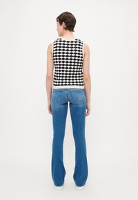 Strikket ermeles topp i krem og marineblå med bølgemønster, parret med lyseblå vide jeans. Bakfra vises ribbestrikket kant og tettsittende silhuett.
