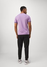 Lila Kurzarmshirt mit schwarzen Akzenten, figurbetontes Design, glatte Textur, kombiniert mit schwarzen Jogginghosen und weißen Sportschuhen.