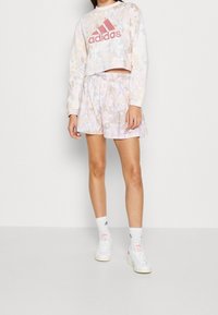 Felpa ritagliata con motivo pastello con logo "adidas" rosa; pantaloncini floreali abbinati; sneakers bianche con accenti discreti; calzini bianchi fino al ginocchio.