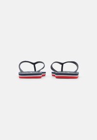 Flip-flops med svarta gummisnören och en texturerad sula. Har en flerskiktad sula med marinblå, vit och röd detalj.