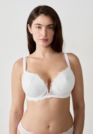 Sujetador de encaje blanco con escote pronunciado, detalles de bordado floral y tirantes ajustables; presenta un diseño con borde en forma de ondas.