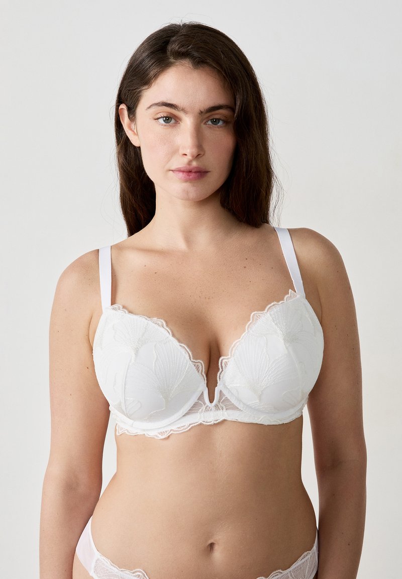Reggiseno bianco in pizzo con scollatura profonda, dettagli di ricamo floreale e spalline regolabili; presenta un design con bordi smerlati.