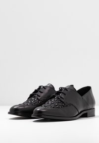 Chaussures noires à lacets avec une tige en cuir lisse et des détails en tissage sur le devant. Petit talon large pour la stabilité et le confort.