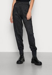 Černé joggingové kalhoty s třpytivou strukturou, elastickým pasem a manžetami, spárované s chunky černými botami.