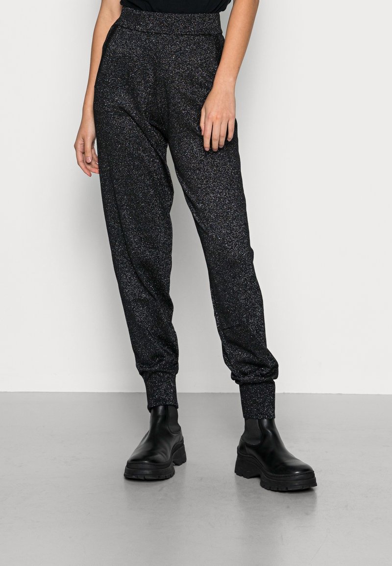 Černé joggingové kalhoty s třpytivou strukturou, elastickým pasem a manžetami, spárované s chunky černými botami.