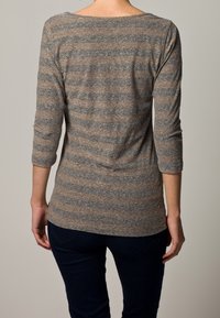 Maglietta a maniche lunghe a righe marroni e grigie con scollo ampio e dettaglio della cucitura sul retro, abbinata a jeans scuri, che mette in evidenza una silhouette aderente.
