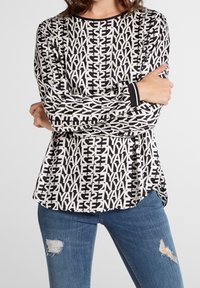 Långärmad topp med ett svartvitt grafiskt textmönster, med rundad halsringning och kontrasterande svarta manschetter, i kombination med slitna blå jeans.