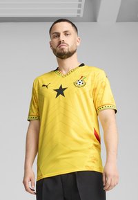 Žltý futbalový dres s čiernou hviezdou a akcentmi, s geometrickými vzormi a dizajnom do v-čka. Logo značky na ľavej hrudi.