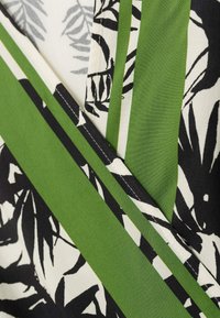 Sukienka z odważnymi zielonymi i czarnymi wzorami liści na białym tle, z kontrastującymi zielonymi paskami i gładką teksturą tkaniny.