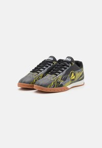 Chaussures de sport avec un dessus à rayures noires et grises, des accents jaunes et une semelle en caoutchouc gomme. Présente un logo rond et un tissu texturé.