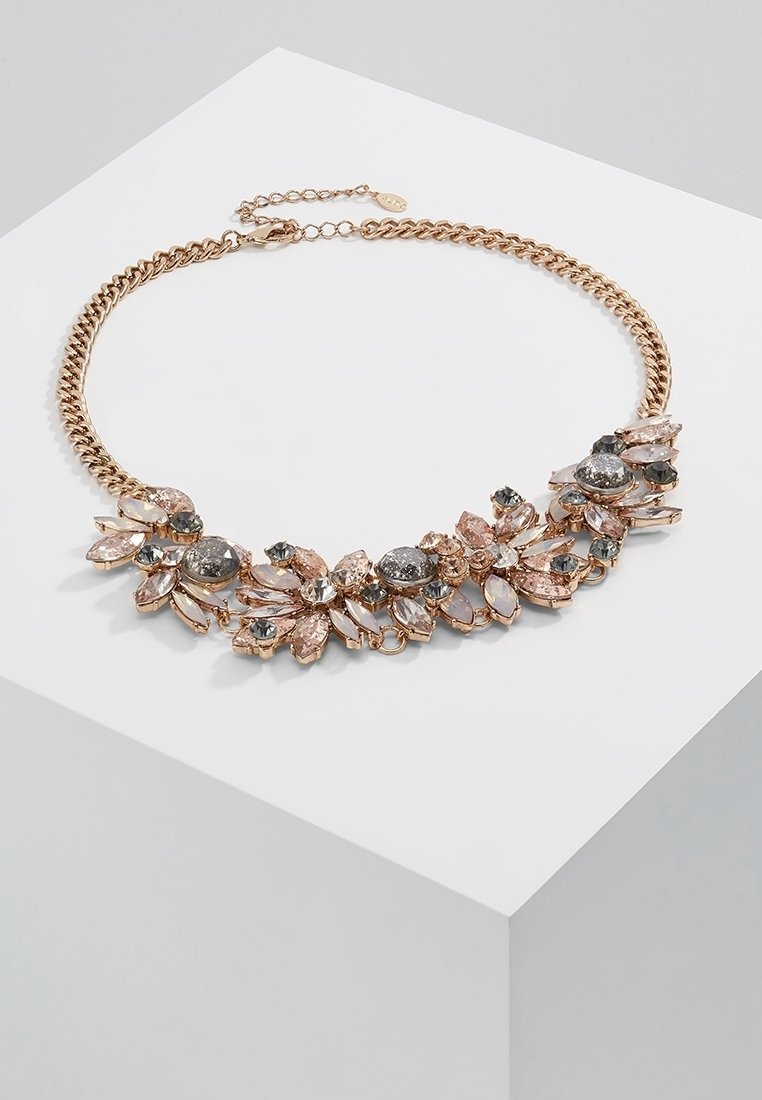 Collier chaîne ton or avec des grappes de pierres précieuses roses et grises scintillantes disposées en motif floral sur une surface blanche.