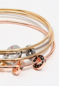 Conjunto de pulseras de metal en dorado, oro rosa y plateado, con un acabado suave. Presenta adornos distintos en algunas pulseras.