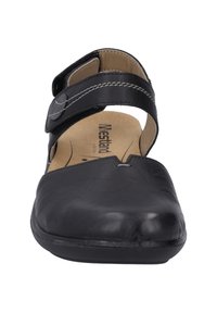 Sandal in pelle nera con cinturino in velcro, lati aperti e punta affusolata. Presenta una soletta interna imbottita e dettagli in cucitura grigia.