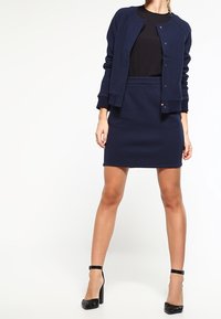 Mörkblå vadderad bomberjacka som matchar en figurnära kjol. Båda plaggen har textilmaterial och jackan har knäppning med knappar.