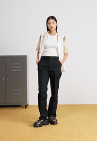 White and beige color-block short-sleeve shirt, white tank top, black tailored pants, and black chunky sandals with a ridged sole.