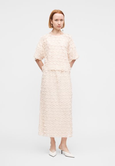Ensemble deux pièces crème brodé de fleurs avec un haut court à manches courtes et une jupe longue assortie. Tissu texturé et coupe droite.
