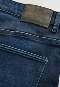 Dark blue denim jeans with a smooth texture, featuring a leather patch at the back waist and visible stitching along the pockets.