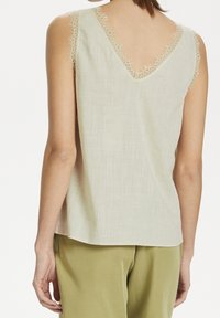 Top in lino senza schienale di un leggero beige con dettagli in pizzo lungo il collo a V e le aperture delle maniche, caratterizzato da una vestibilità comoda e un orlo leggermente curvo.