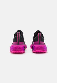 Nike løbesko med sort stofoverdel, pink accenter og en tyk, tekstureret sål. Har en pull-tab og logo på hælen.